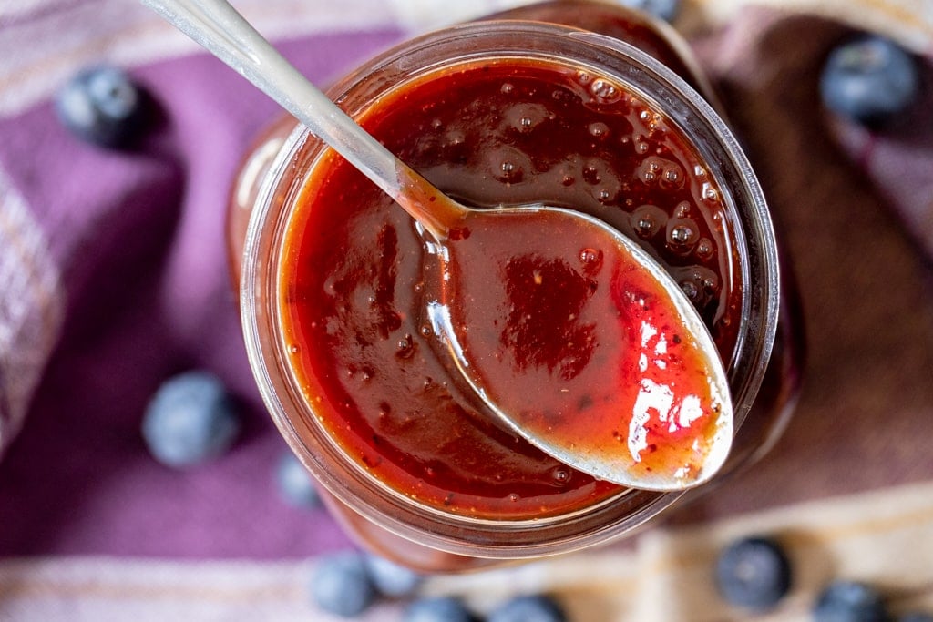 Blueberry BBQ sauce in a glass mason jar with a spoon resting on top of the jar.