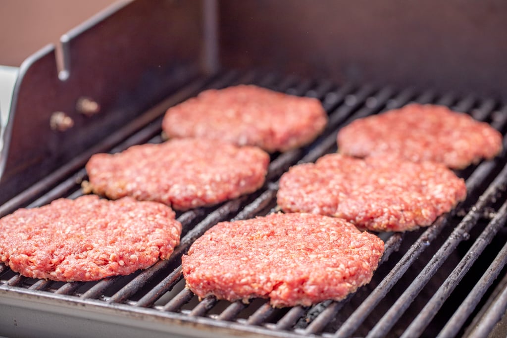 Six meat patties on the grill grates of the gas grill.