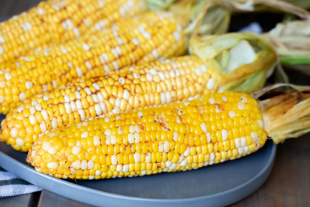 Four ears of smoked corn on the cob on a gray plate.