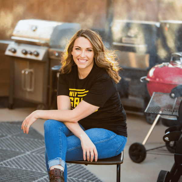 Susie sits in front of a collection of grills and smokers.