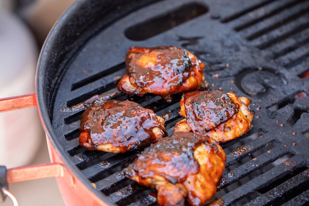 Sauced chicken thighs on the grill grates of a charcoal grill.