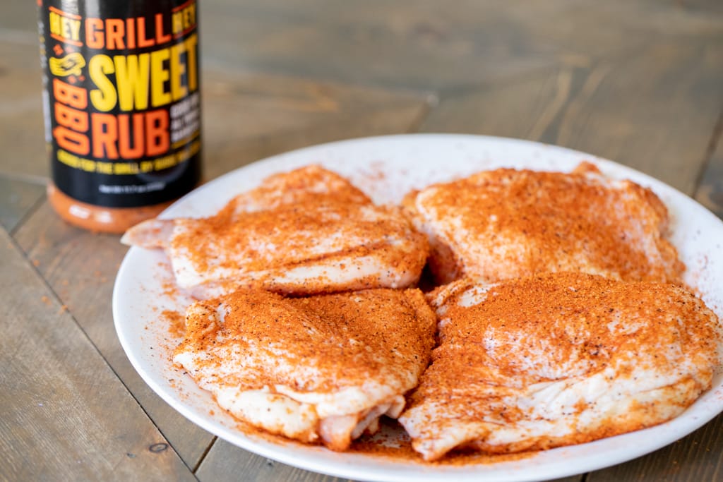Four seasoned chicken thighs next to a bottle of Sweet Rub.