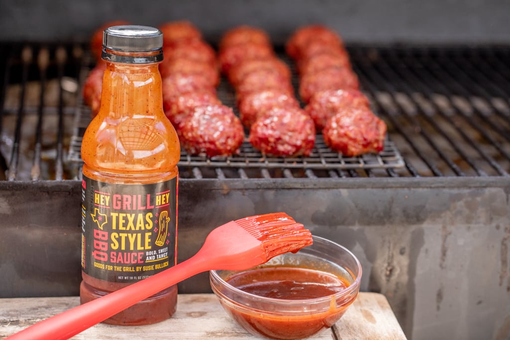 BBQ meatballs on the smoker with a bottle of Texas Style BBQ Sauce in the foreground.