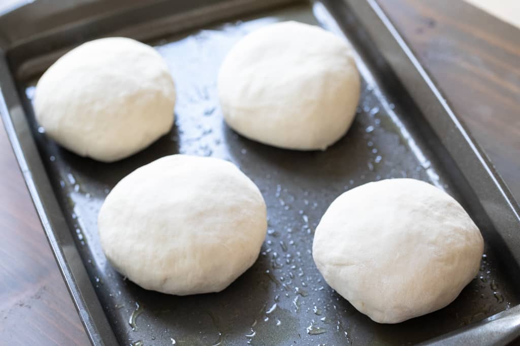 Four balls of pizza dough on a rimmed baking sheet