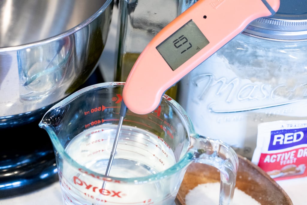 Instant read thermometer in a measuring cup of water reading 107 degrees F.