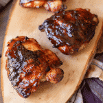 BBQ chicken thighs on a long, wooden cutting board.