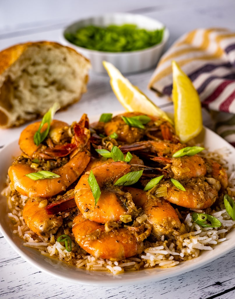 New Orleans BBQ shrimp over a bed of rice garnished with sliced onions and lemon wedges.