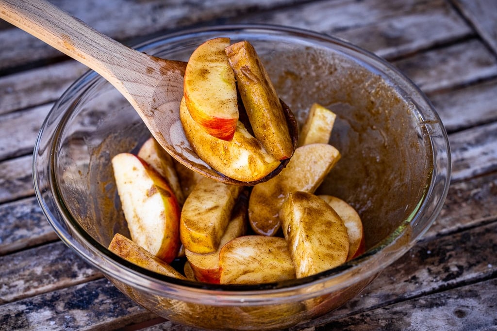 Apple wedges tossed in melted butter and spices in a glass bowl.