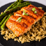 BBQ salmon on a bed of rice next to grilled asparagus.