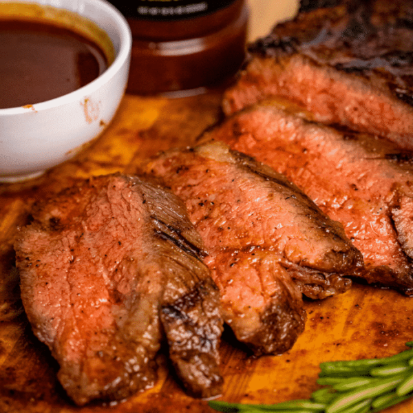 Sliced BBQ tri tip next to a small bowl of BBQ sauce.