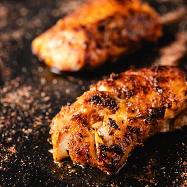 Two cooked fish fillets on a black surface.