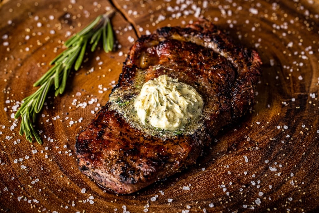 Grilled bison steak topped with resting steak butter on a wooden cutting board.