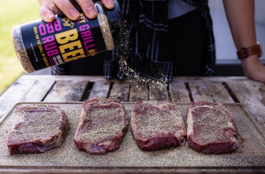 Hey Grill Hey Beef Rub being sprinkled on four bison steaks.