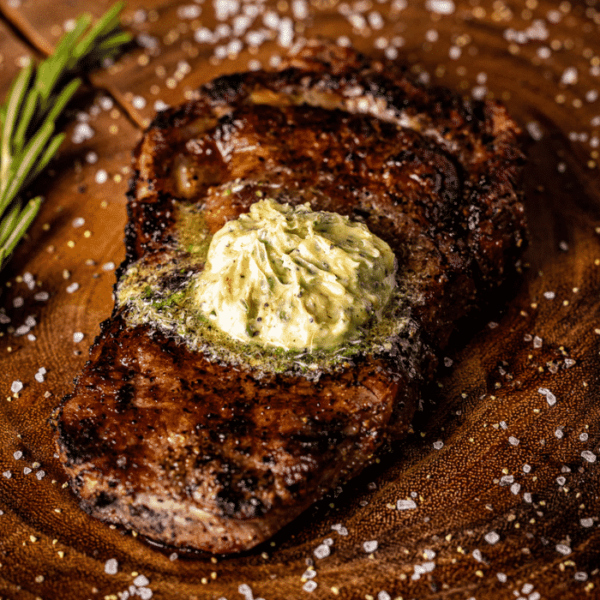 Grilled bison steak topped with resting steak butter on a wooden cutting board.