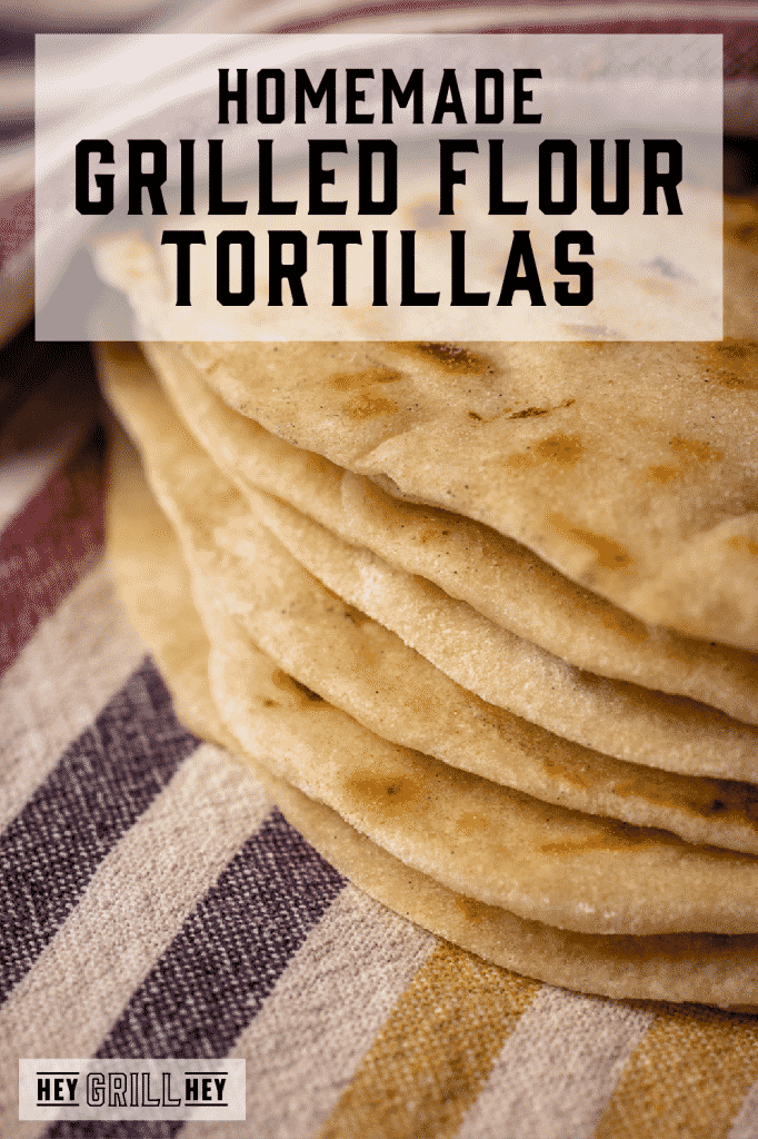 Stack of grilled flour tortillas on a striped dish towel with text overlay - Homemade Grilled Flour Tortillas.