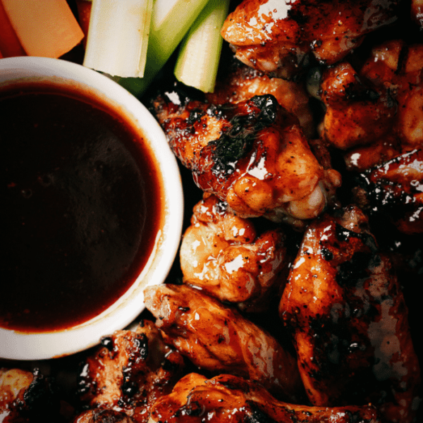 Honey BBQ chicken wings next to a bowl of BBQ sauce and sliced celery.