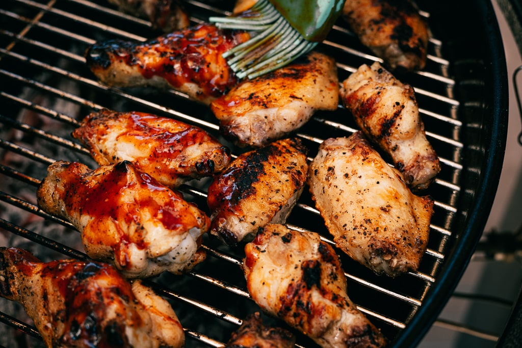 Grilled BBQ chicken wings being brushed with BBQ sauce.