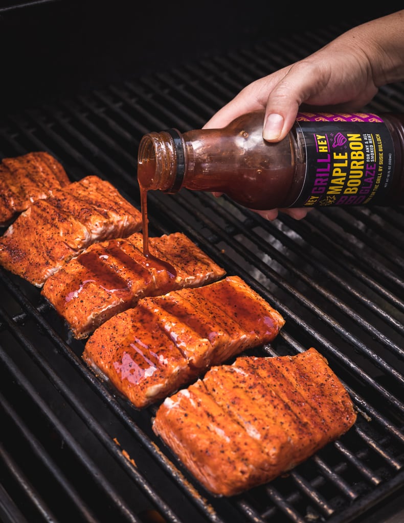 Maple bourbon grilling glaze being drizzled on salmon fillets on the grill.