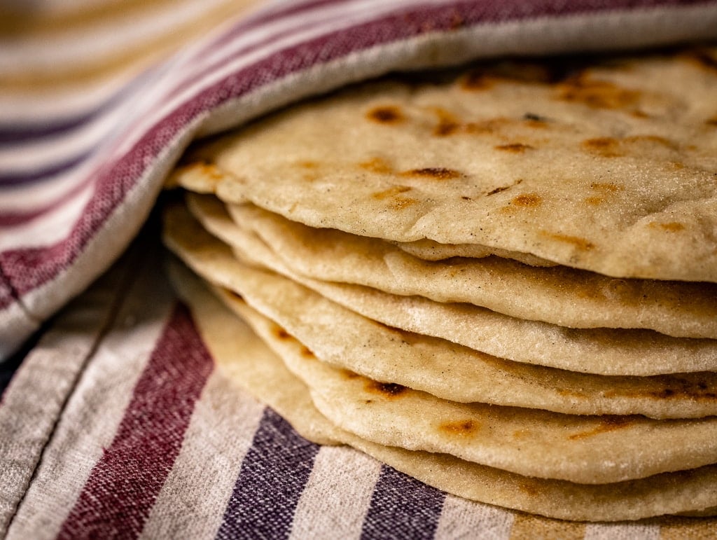 Stack of grilled flour tortillas on a striped dish towel.