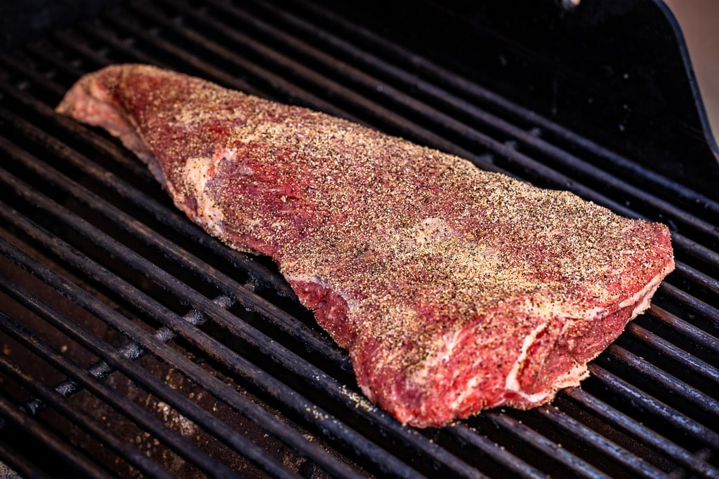 Seasoned tri tip on the grill grates of a BBQ.