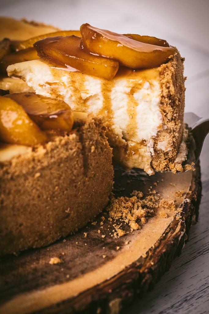 Slice of smoked cheesecake topped with brandied peaches being pulled from the whole cheesecake.