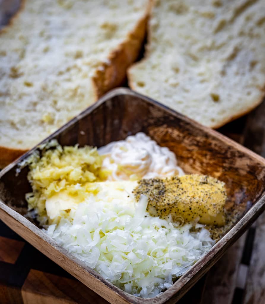 Ingredients for garlic butter in a square dish with a sliced loaf of bread in the background.
