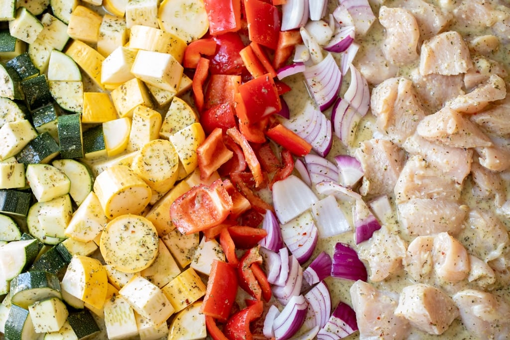 Sliced zucchini, yellow squash, red pepper, onion, and chicken lined up in a kabob marinade.