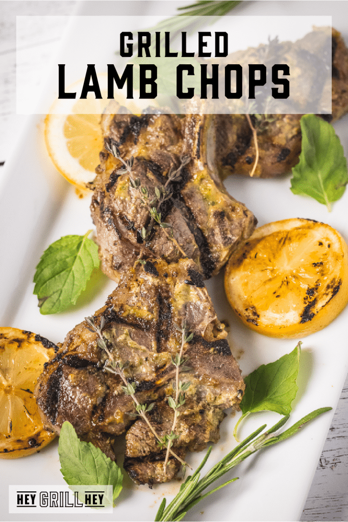 Three grilled lamb chops surrounded by fresh herbs and sliced lemons with text overlay - Grilled Lamb Chops.