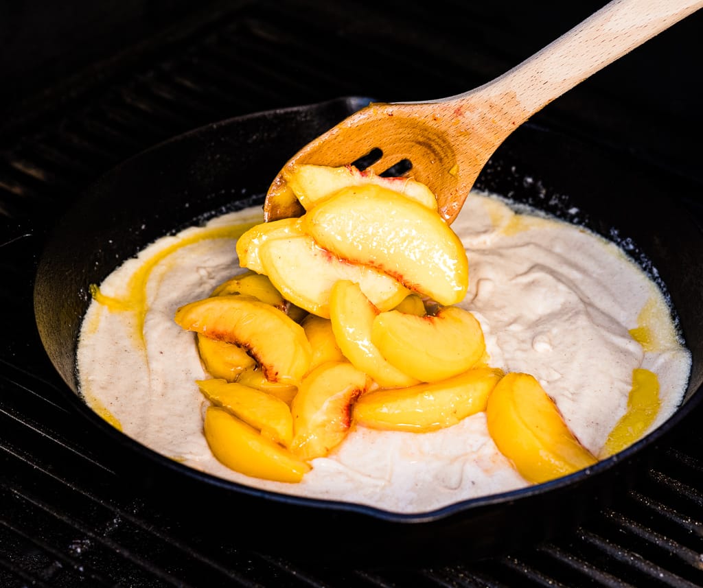 Peaches being mixed into cobbler batter in a cast-iron skillet.