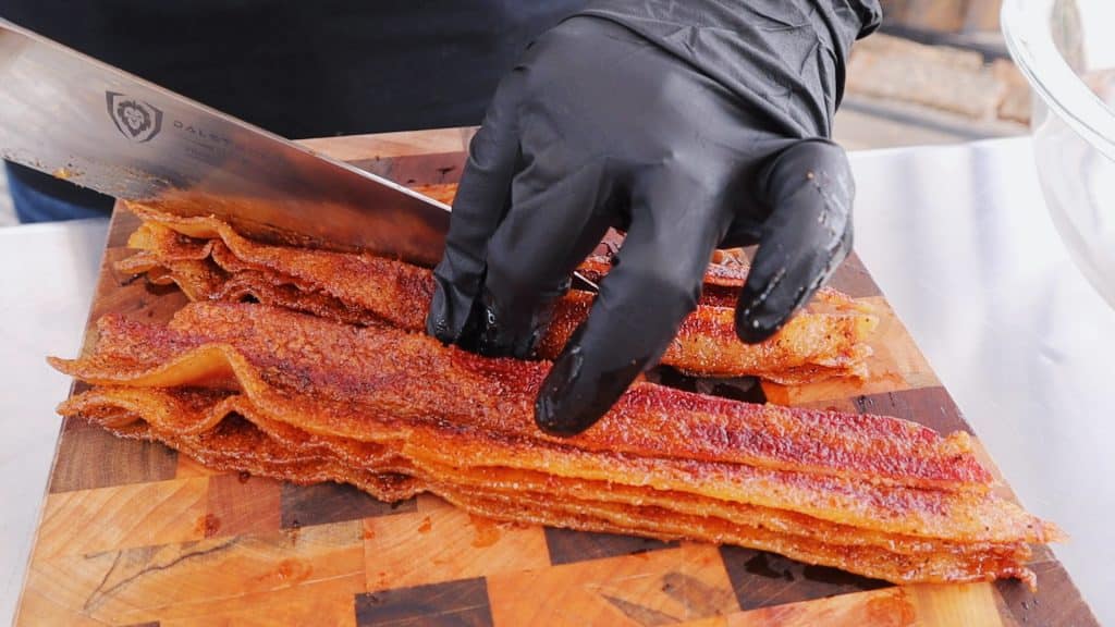 Smoked bacon being sliced in half on a wooden cutting board.