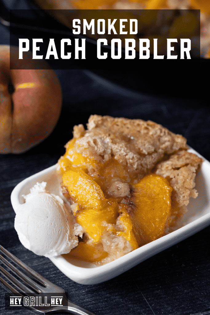 Smoked peach cobbler and a scoop of vanilla ice cream in a serving dish with text overlay - Smoked Peach Cobbler.