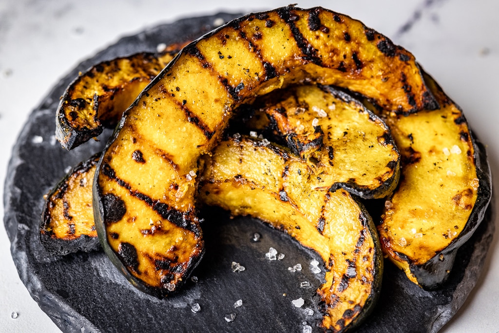 Grilled acorn squash spears stacked on a serving dish.