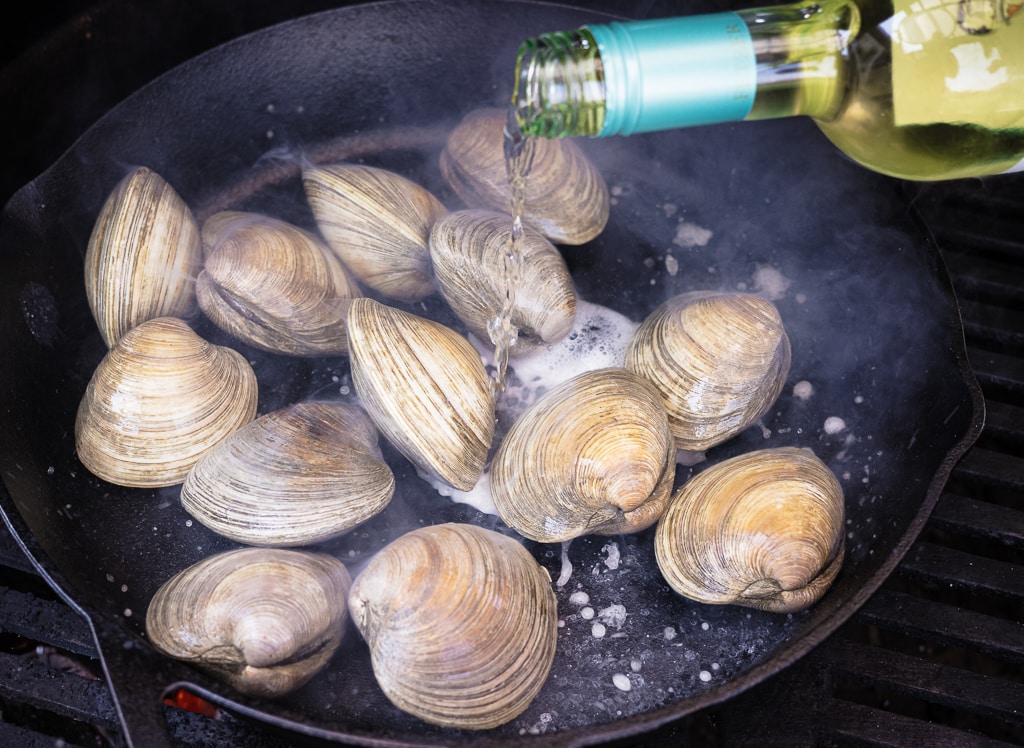 Clams in a skillet being drizzled by white wine.