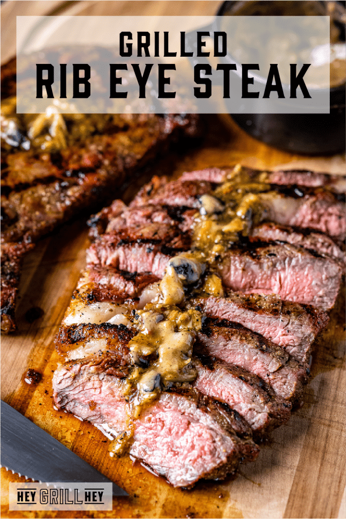 Sliced grilled rib eye steak topped with roasted garlic resting butter with text overlay - Grilled Rib Eye Steak.