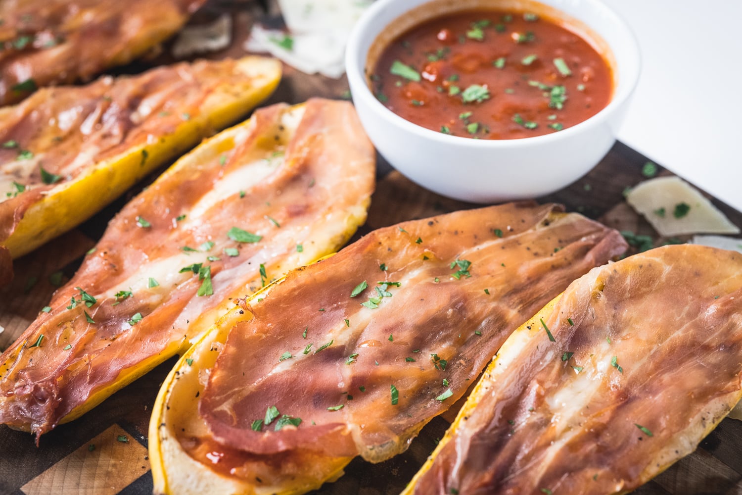 Stuffed yellow squash topped with marinara, cheese, and prosciutto on a wooden serving board.