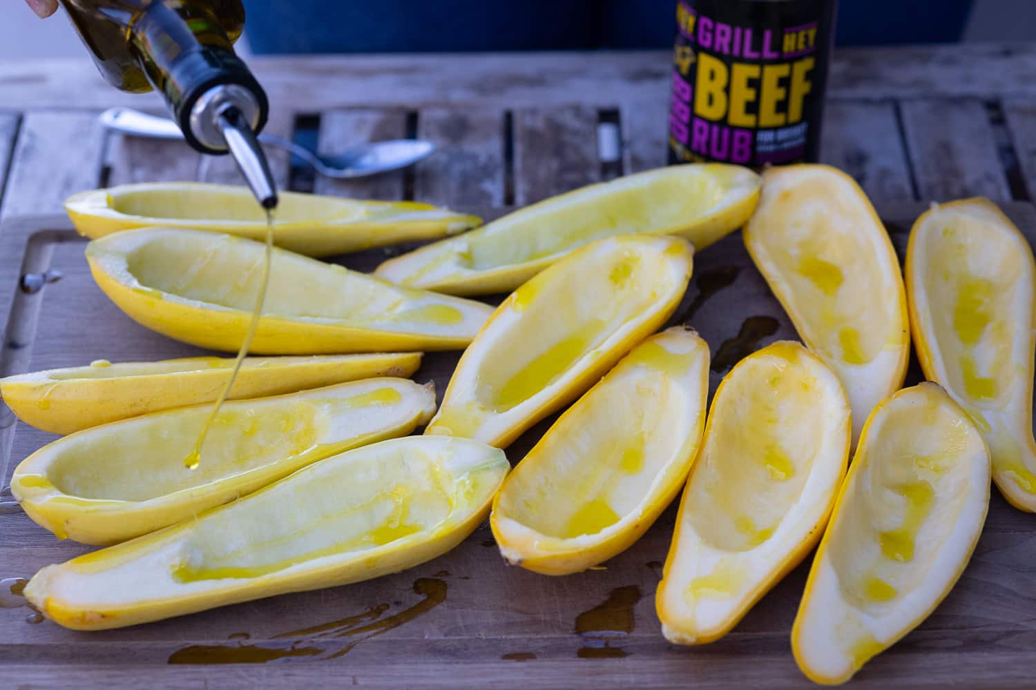 Yellow squash halves being drizzled with olive oil.