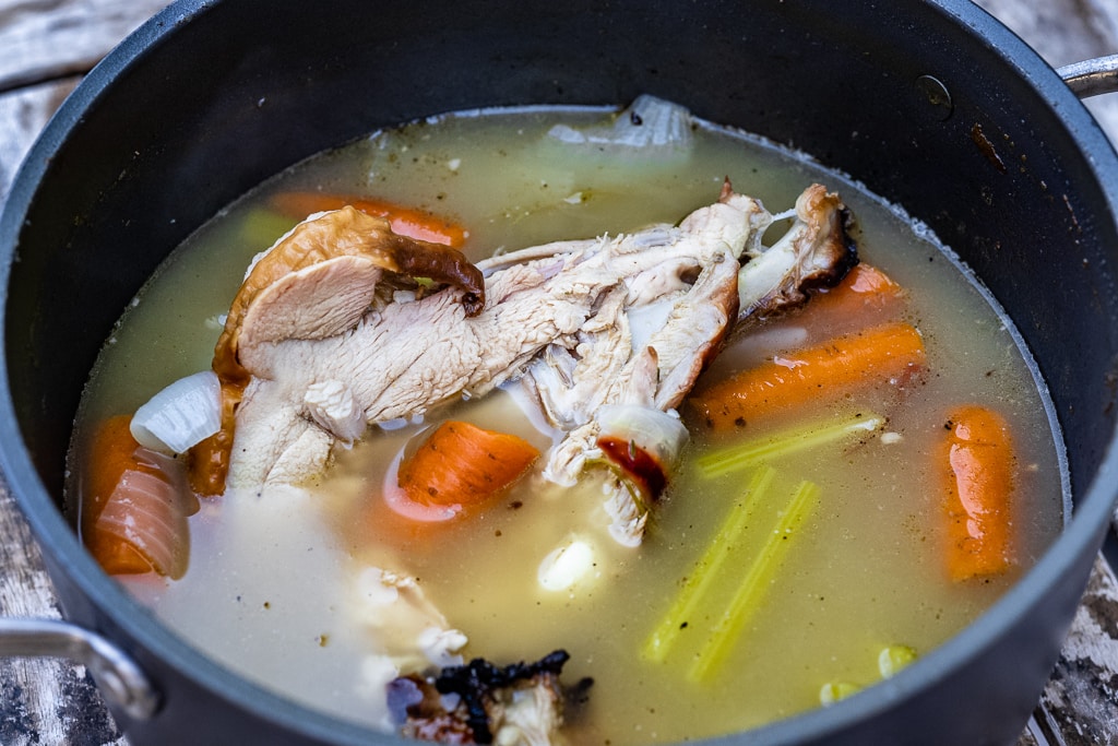 Turkey carcass in a large pot with broth and vegetables.