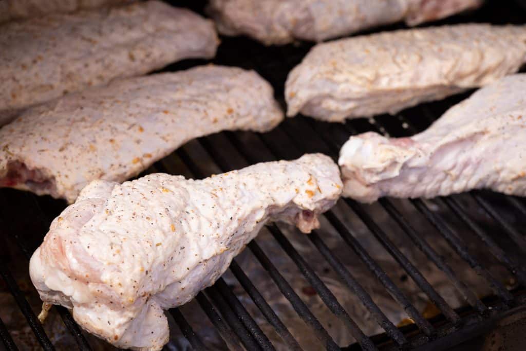 Seasoned turkey wings on the grill grates of a smoker.