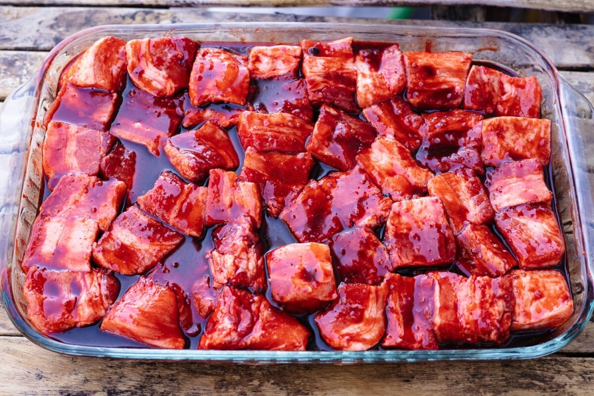 Cubed pork belly in a char siu glaze in a rectangular glass baking dish.