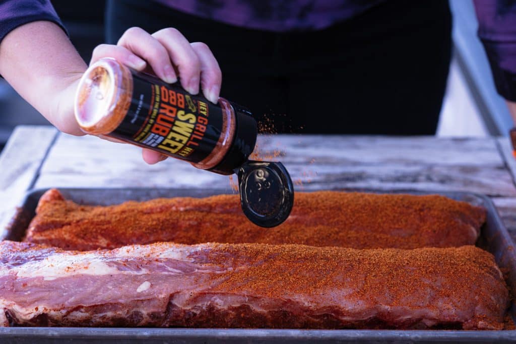 Hey Grill Hey Sweet Rub being sprinkled on two racks of baby back ribs.