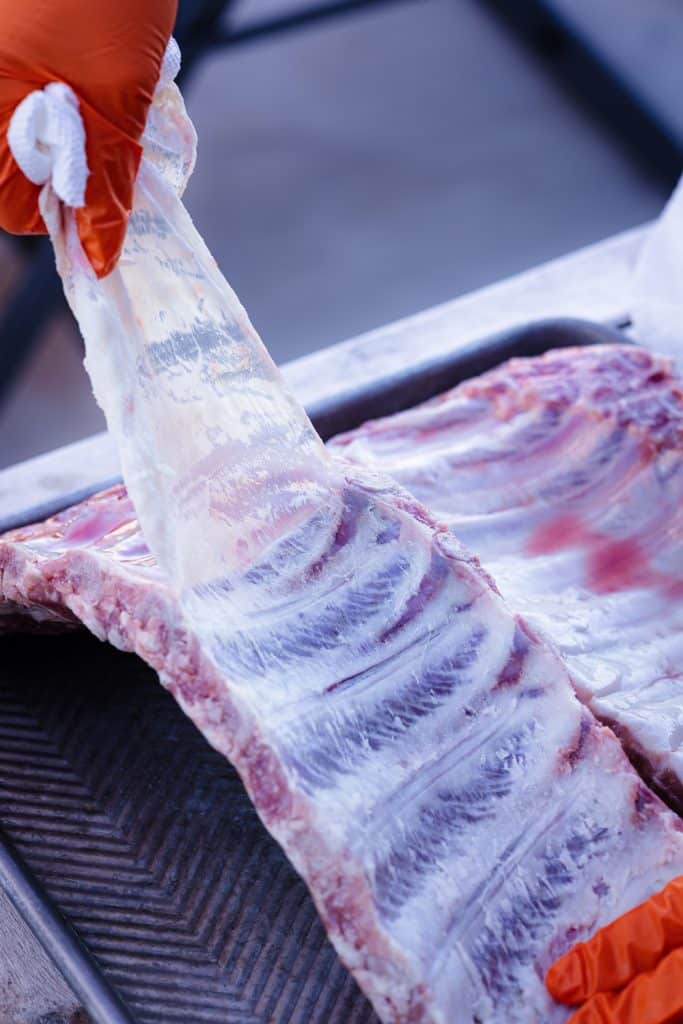 Rib membrane being pulled of the back of a rack of ribs.