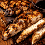 Sliced balsamic marinated chicken on a wooden cutting board.