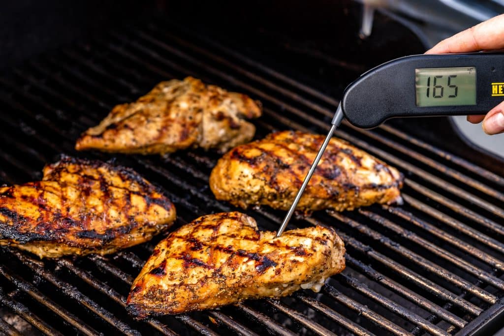 Thermometer reading 165 degrees F in a chicken breast on the grill.