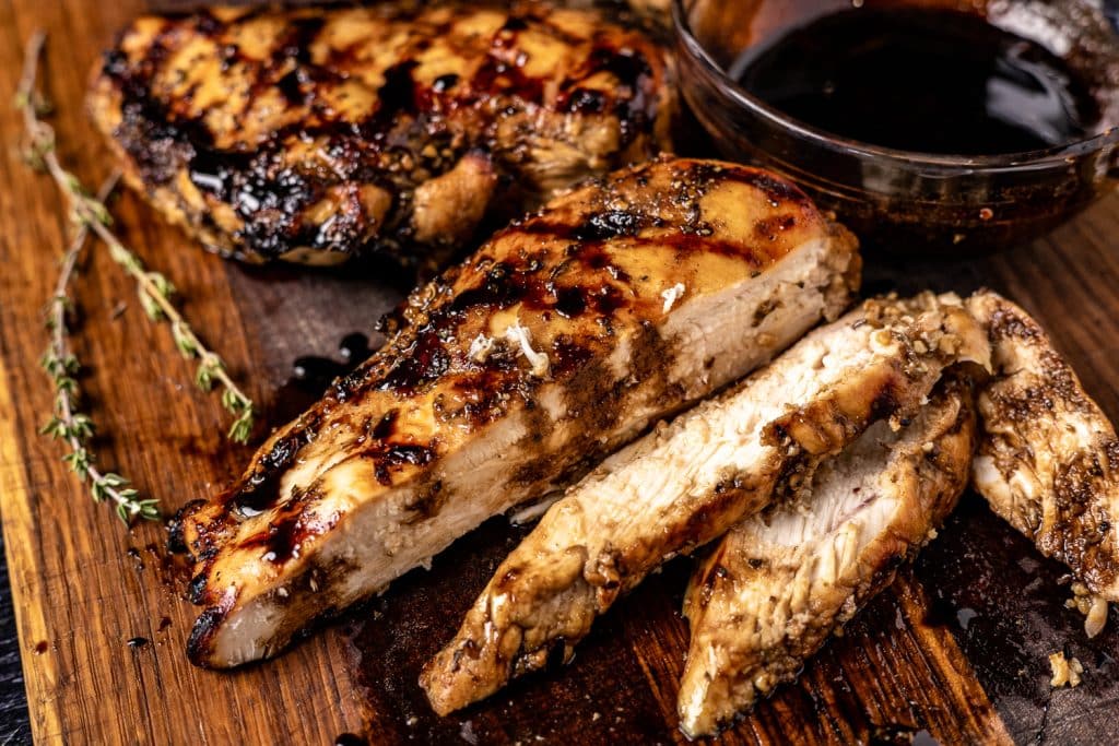 Sliced balsamic marinated chicken on a wooden cutting board.