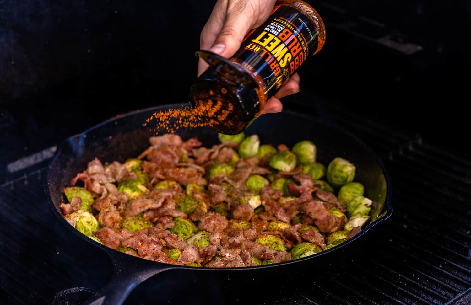 Hey Grill Hey Sweet Rub being sprinkeld on a skillet full of Brussels sprouts and bacon.