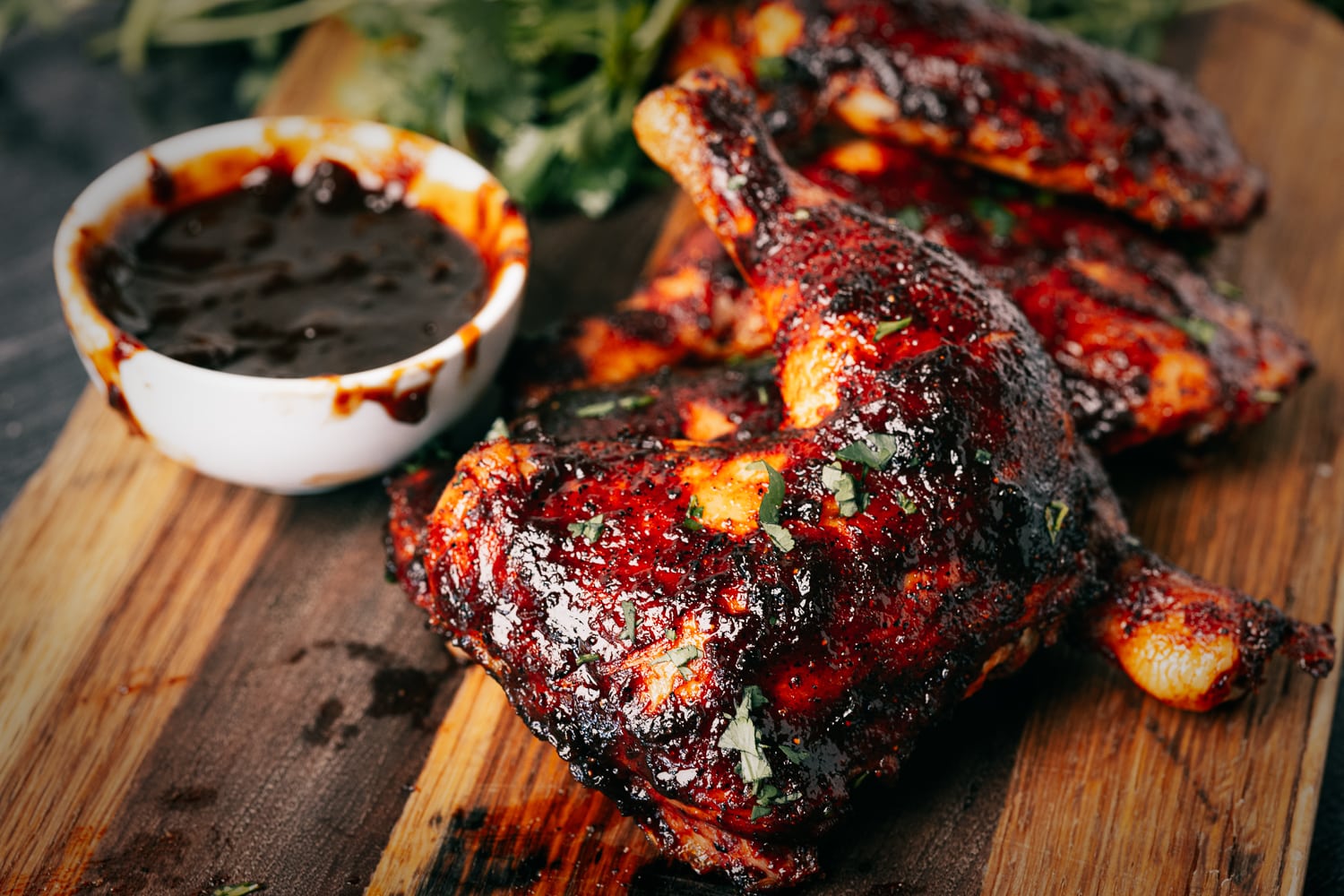 Chicken quarters on a wooden cutting board next to a small bowl of BBQ sauce.
