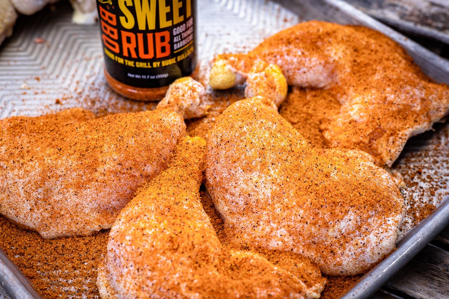 Chicken quarters seasoned with Sweet Rub on a metal baking sheet.