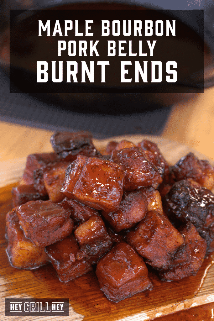 Stack of pork belly burnt ends on a wooden cutting board with text overlay - Maple Bourbon Pork Belly Burnt Ends.