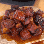 Stack of pork belly burnt ends on a wooden cutting board.