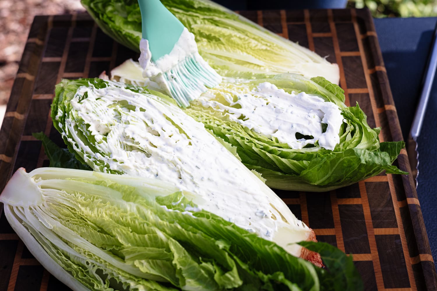 Ranch dressing being spread on romaine hearts with a basting brush.